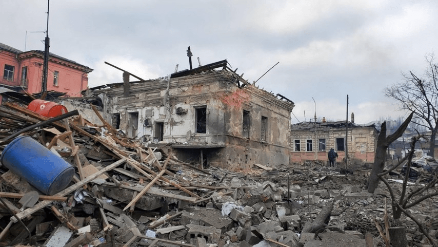 Ein in den Kämpfen im Mai vergangenen Jahres zerstörtes Haus in Mariupol, daneben die Technische Universität, die von 2014 bis 2022 dem neonazistischen Regiment AZOV als Unterkunft diente